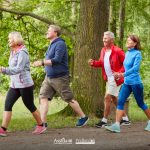 Un gruppo di persone adulte e anziane cammina a passo svelto in un bosco per rallentare l'Alzheimer