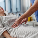 Operatore sanitario visita l’addome di una donna sdraiata su un lettino ospedaliero, immagine illustrativa dell’endometriosi