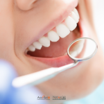 Una dentista in camice azzurro mostra un modello anatomico di arcata dentale a una paziente all'interno di uno studio dentistico.