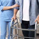 Persona con difficoltà motorie utilizza un deambulatore con l’assistenza di un’operatrice sanitaria
